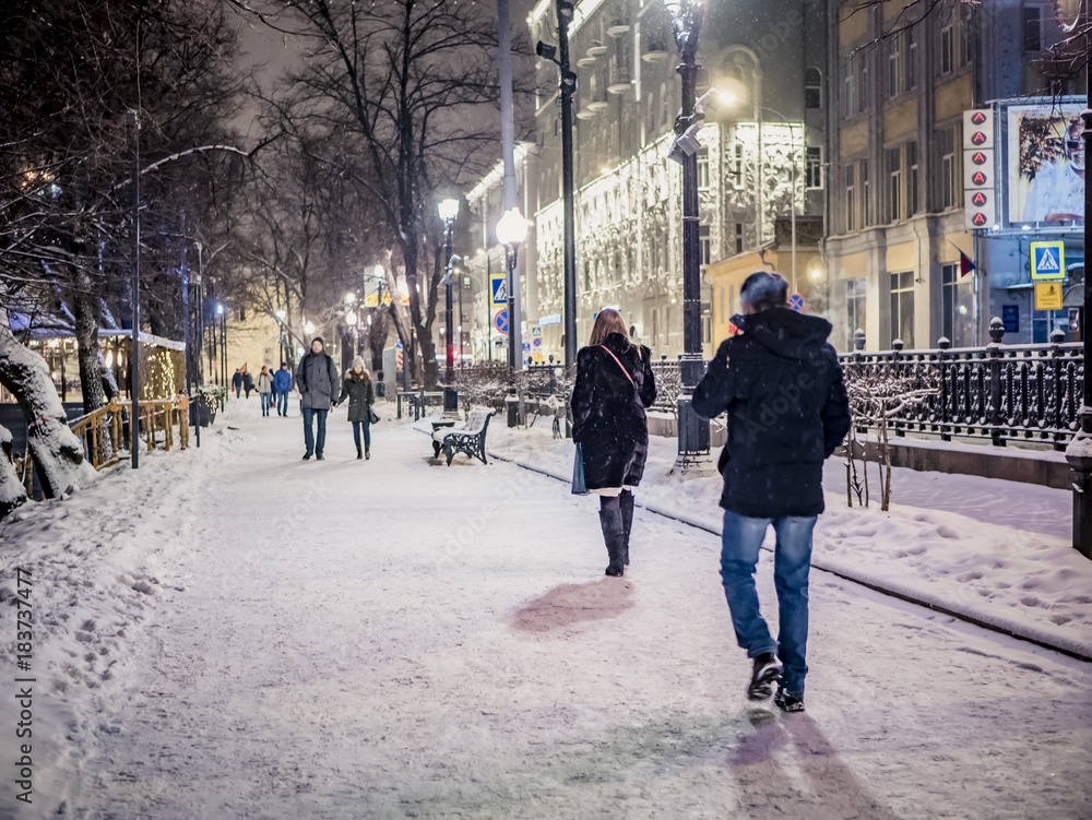 night snowy winter landscape in the alley of city park with walking ...
