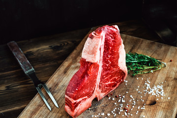 raw t bone steak on wooden Board and black background