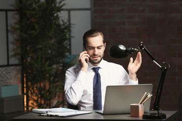 Canvas Print - Tired young man with laptop and cell phone in office at night