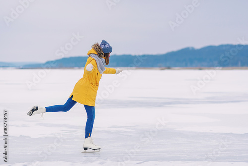 Fotografía Young beautiful girl in yellow jacket is skating at winter on a frozen lake