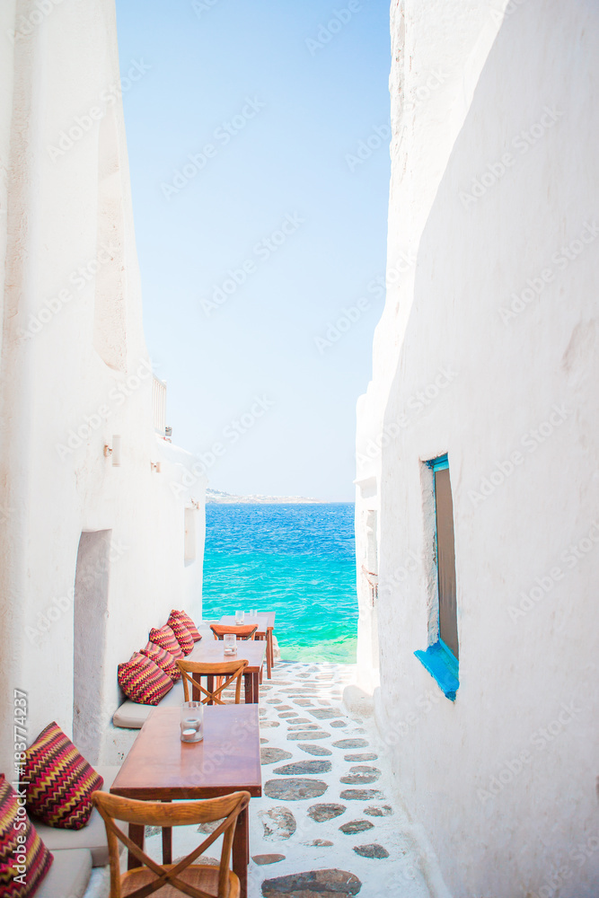 Benches with pillows in a typical greek outdoor cafe in Mykonos with amazing sea view on Cyclades islands - obrazy, fototapety, plakaty 