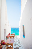 Fototapeta Uliczki - Benches with pillows in a typical greek outdoor cafe in Mykonos with amazing sea view on Cyclades islands