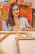 Beautiful woman painter behind of empty frame, in a studio paint background