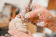Close up of man ceramist hands holding a tool and working on sculpture details of the head on wooden table in workshop