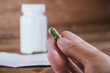 © nokturnal - Hand hält medizinische Cannabis Kapsel weiße Tablettendose im Hintergrund