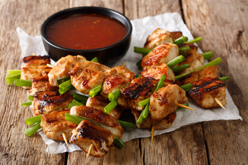 Wall Mural - Asian spicy chicken skewered with green onion and chili sauce close-up. horizontal