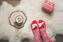 Woman In Warm Christmas Knitted Socks Wants To Drink Coffee And Open A Gift. Top View.