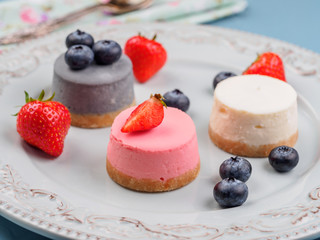 Wall Mural - Small round berry cheesecakes on plate and blue background