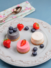 Wall Mural - Small round berry cheesecakes on plate and blue background