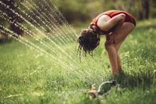 Girl Playing In A Sprinkler In The Backyard