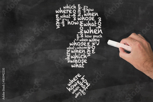 Valokuva hand holding piece of chalk writing question words in shape of question mark on