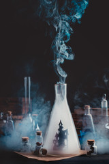 Wall Mural - Lab bottle with haunted castle silhouette. Wizard workplace with smoke and magical equipment. Dark conceptual still life.