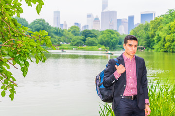 Wall Mural - Wearing black blazer, red, white patterned under shirt, carrying shoulder bag, young college student standing by green lake in big city, confidently looking at you. Concept of Environment Protection..