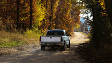 White Pickup Truck Driving Down Dusty Dirt Road With Fall Leaves And Dust Behind