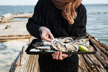 Young Woman Holding Metal Tray Of Open Oysters Ready For Consuming On Sea Shore, Outdoor