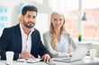 © pressmaster - Two successful colleagues in formalwear looking at camera by their workplace in office