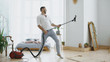 © silverkblack - Young man having fun cleaning house with vacuum cleaner dancing like guitarist