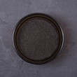 Black cumin powder in a bowl on a grey concrete background