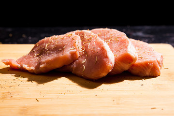 Close up on uncooked meat seasoned with spices, salt and pepper on wooden board