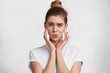 © WHstudio Leushin N - Indoor shot of beautiful blue eyed female model with hair bun, dressed in white casual clothes has puzzled expression, sees something unexpected, isolated over white concrete background. Body language