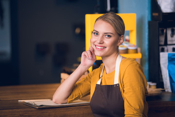 Wall Mural - Portrait of happy female barista situating near table while leaning elbow on it in confectionary shop. Job concept