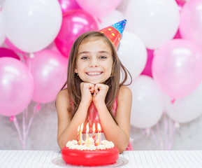  happy girl in party hat with birthday cake looking at camera