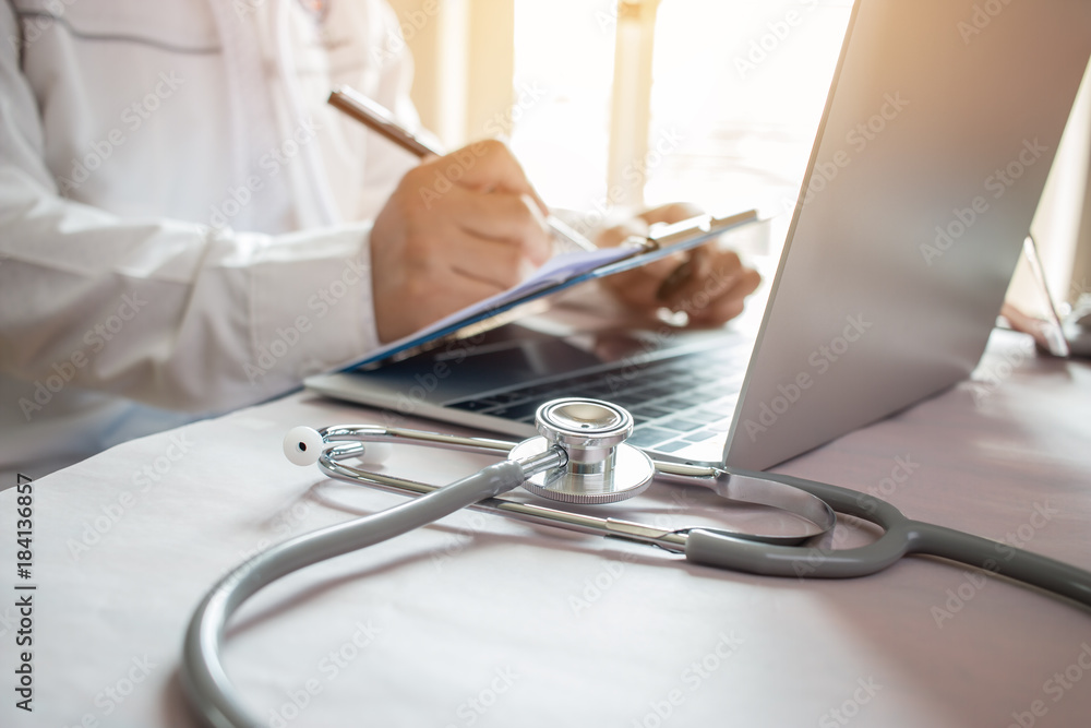 Medicine doctor's writing on laptop in medical office.Focus stethoscope on foreground table in hostpital.Stethoscope is acoustic medical device for auscultation,listening internal sounds of human body