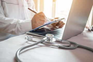 Medicine doctor's writing on laptop in medical office.Focus stethoscope on foreground table in hostpital.Stethoscope is acoustic medical device for auscultation,listening internal sounds of human body