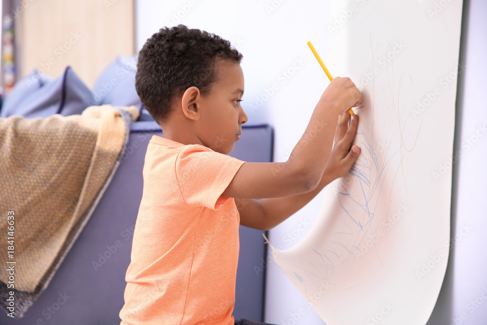 Little African-American boy drawing on paper roller indoors