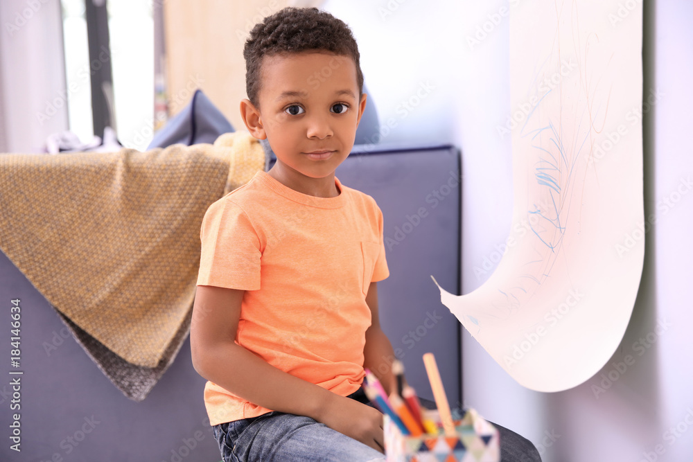 Little African-American boy drawing on paper roller indoors