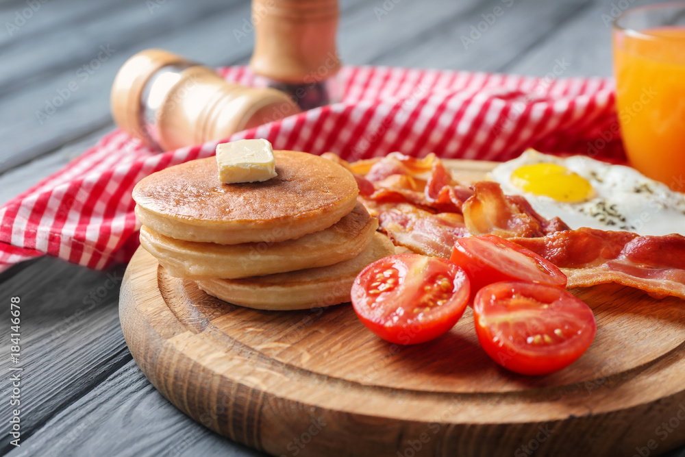 Board with yummy pancakes, tomatoes, fried bacon and egg on wooden table