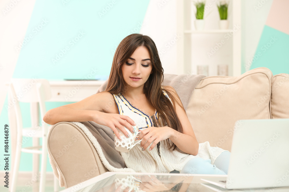 Young woman with cup of tea on sofa at home