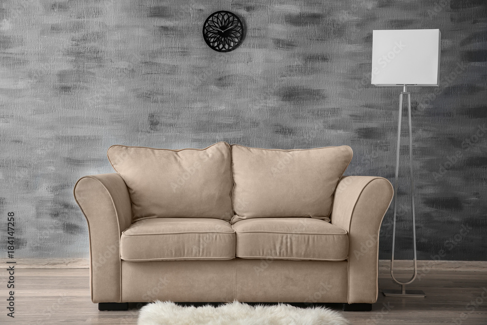 Stylish sofa with lamp near wall indoors