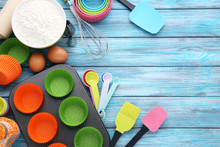 Empty Cupcake Cases With Different Kitchen Utensils On Wooden Table