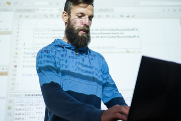 programmer courses at education center. Man looking in laptop while lecturing on information and communications technology. His presentation in the background