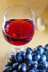 Close up view of a glass of red wine next to bunch of black grapes and a cork on a wooden table (concept, shallow depth of field)