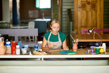 Canvas Print - Portrait of pretty blonde woman enjoying work in art studio painting picture on wood making DIY decor, copy space