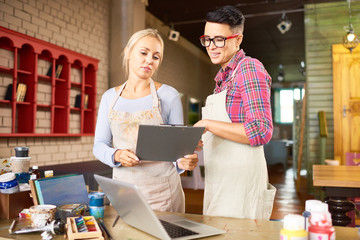 Canvas Print - Portrait of two creative young women  working together in art studio holding clipboard and planning new  crafting project