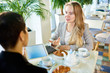 © Seventyfour - Portrait of two modern young women discussing work sitting at table in cafe during business meeting during breakfast, focus on young blond trainee talking enthusiastically