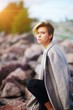 © raisondtre - blonde woman with short hair sitting on a rock on the beach in coat