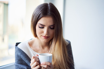 Calm young woman drinking coffee sitting cosily at home