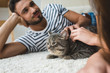 © LIGHTFIELD STUDIOS - young couple petting cat while lying on floor at home