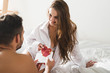 © LIGHTFIELD STUDIOS - man giving valentines day greeting card to girlfriend in bed