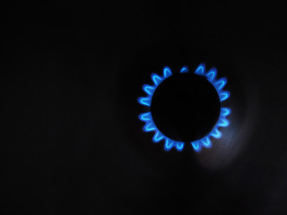 Burning gas stove hob, blue flames close-up in the dark on a black background. Gas burner top view