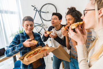 multicultural friends standing and eating pizza