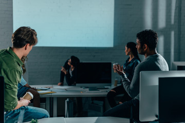 Wall Mural - People watching presentation in office at nighttime. blank screen