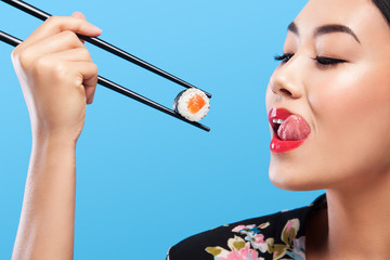 Asian woman with sushi eating sushi and rolls on a blue background