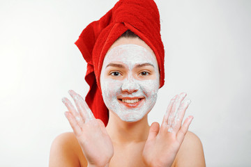 Wall Mural - happy beautiful girl with a red towel on her head applies a scrub on the face of a large portrait on a white background