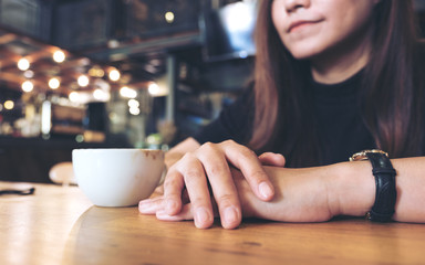 Closeup image of a woman clap one's  hand , sitting and thinking in cafe with a white cup of coffee on wooden table