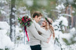 Cute couple in beige knitted pullovers in snowy forest. Newlyweds is touching foreheads. Winter wedding